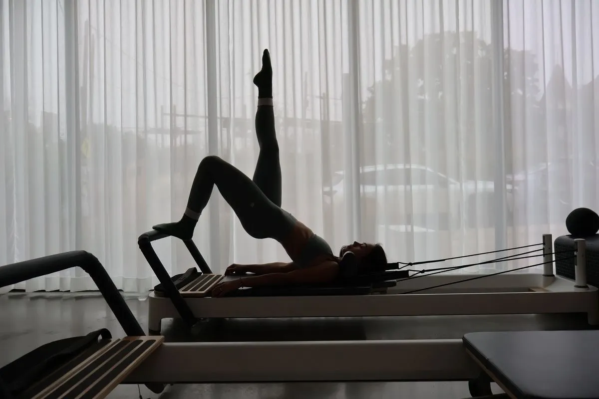 Une pratiquante sur un reformer, en contre-jour devant les rideaux de la salle 1